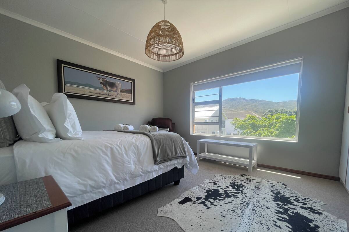 A bedroom with a large bed, a window with a mountain view, a rattan ceiling light, and a framed picture on the wall.