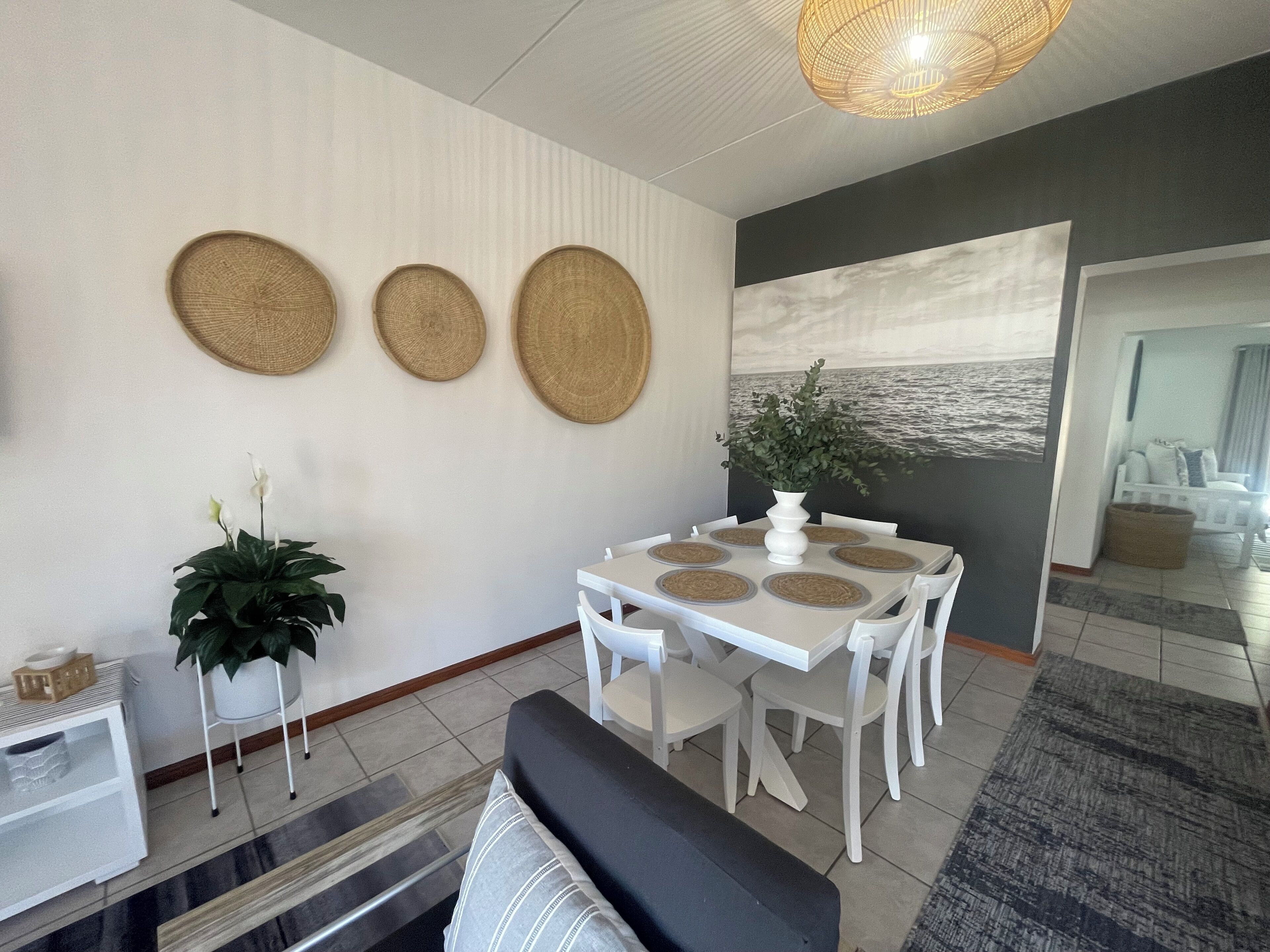 Een eethoek met een witte tafel en stoelen, een potplant en een wand met drie geweven placemats.