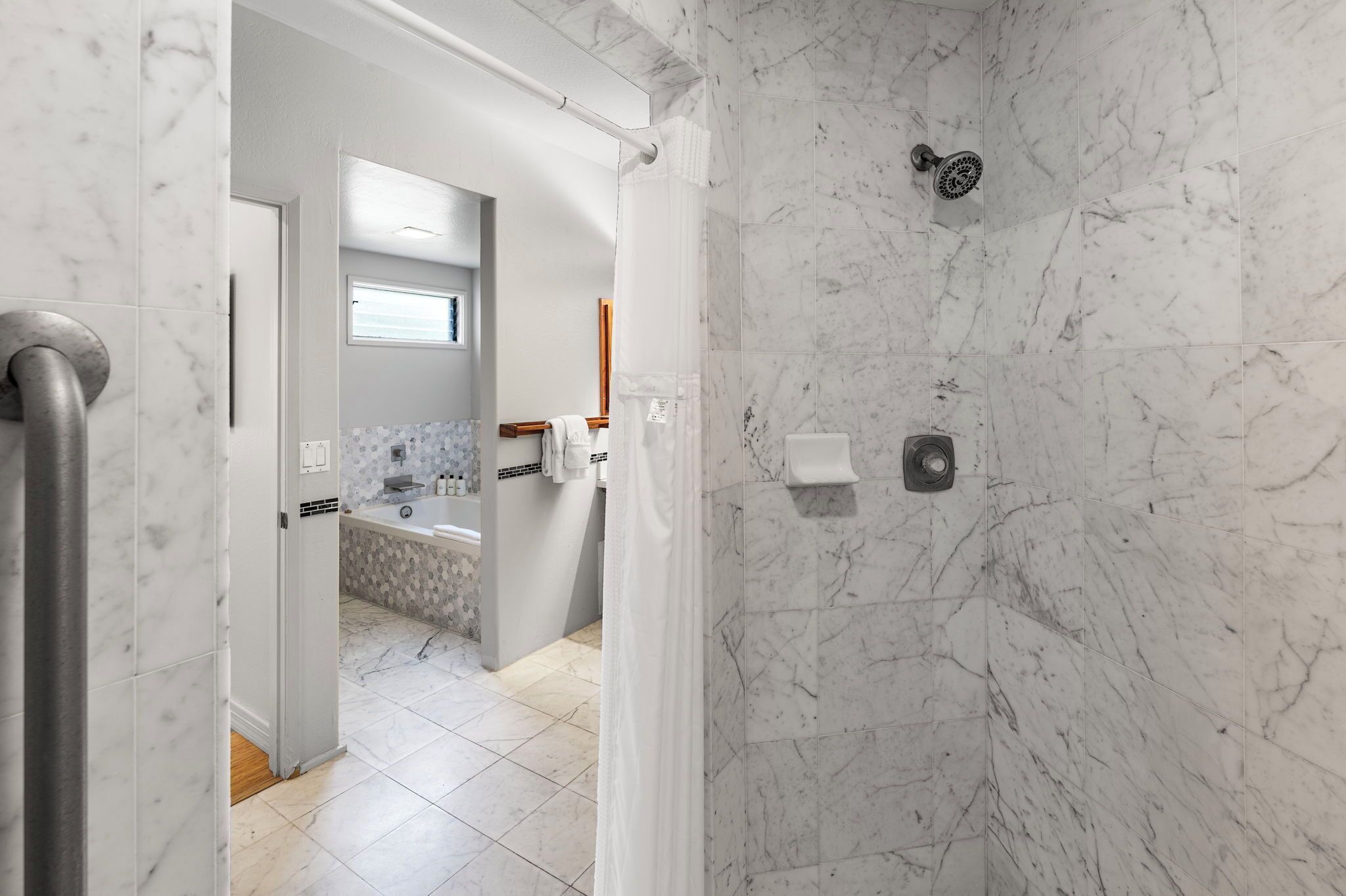 A modern bathroom with a shower, marble walls, and a visible toilet paper holder.