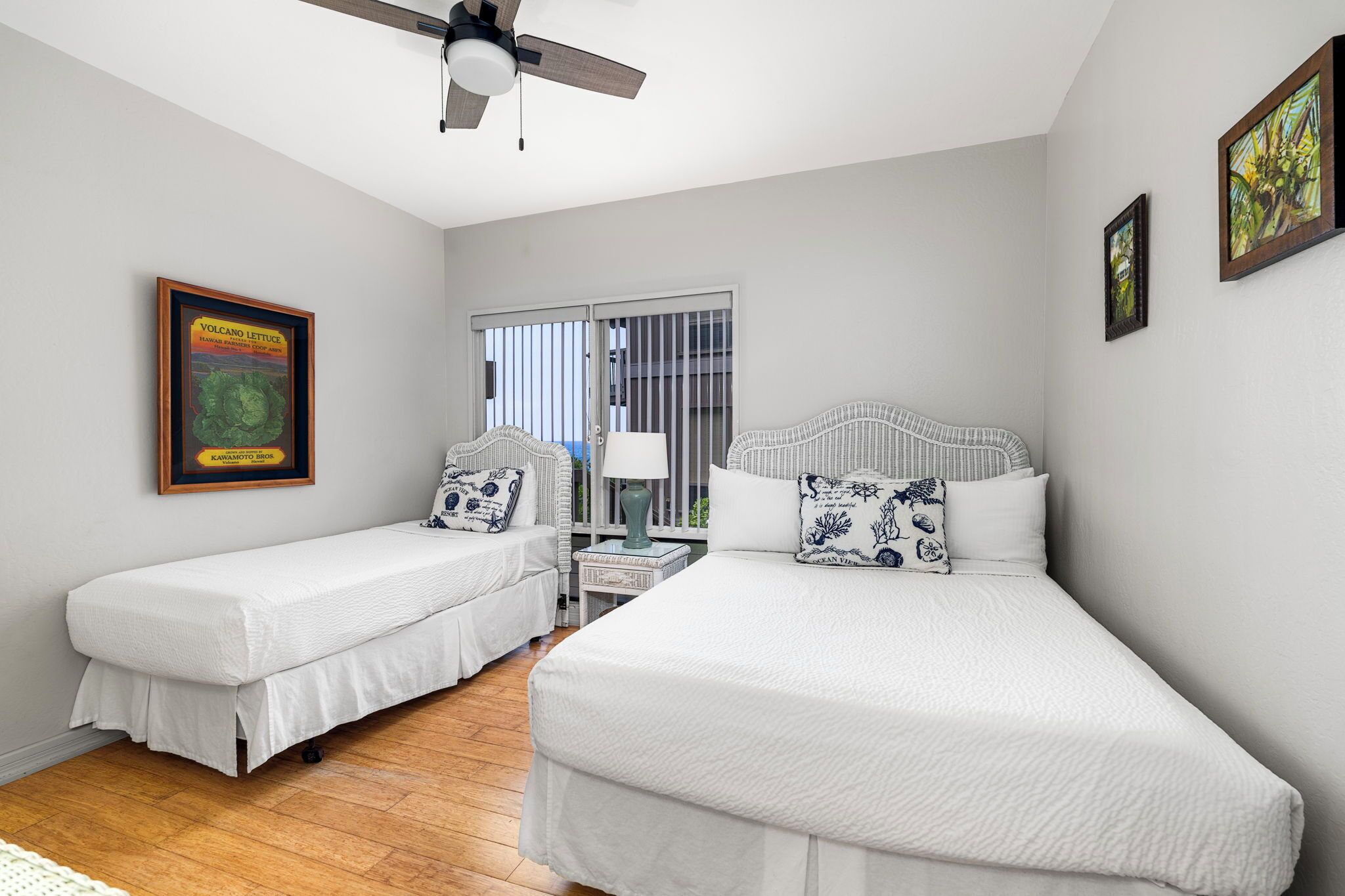 A bedroom with two single beds, a ceiling fan, a window with blinds, and a framed picture on the wall.