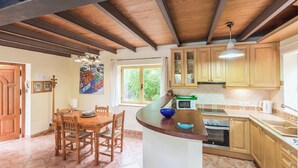 Een keuken met houten kastjes, een eettafel met stoelen, een magnetron en een spoelbak.