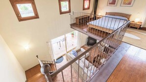 Een kamer met meerdere niveaus, een houten trap, een bed, een open haard en een balkon met buitenmeubilair.
