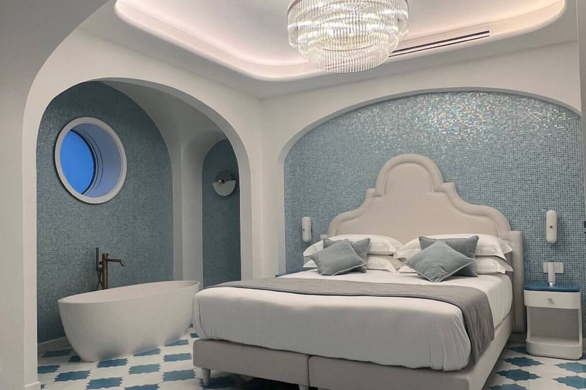 Een moderne slaapkamer met een groot bed, een ronde spiegel, een bad en een kroonluchter.