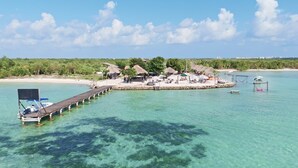 A resort with a pier extending into clear turquoise waters, surrounded by lush greenery and thatched-roof structures.