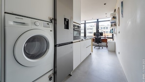 Een moderne keuken met een Samsung wasmachine, een koelkast en een raam dat natuurlijk licht binnenlaat.