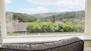 Une vue depuis une fenêtre, avec un coussin gris au premier plan, donnant sur un paysage composé de bâtiments et de verdure.