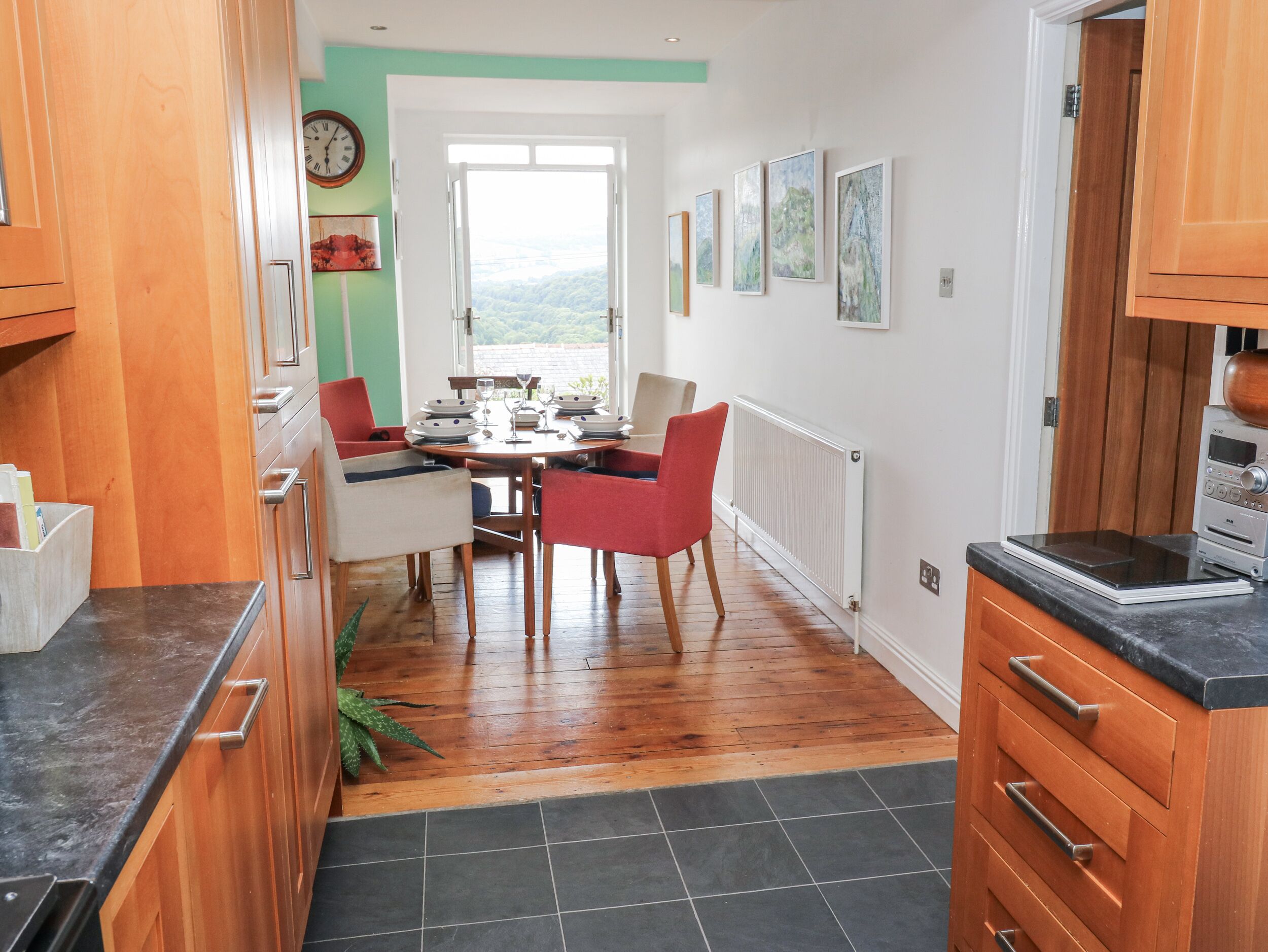 A modern kitchen with wooden cabinets, a dining table set for four, and a view through a large window.