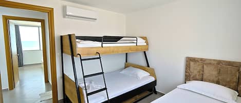 A bunk bed with a wooden frame, white bedding, and a headboard. There is a door leading to another room and an air conditioning unit on the wall.