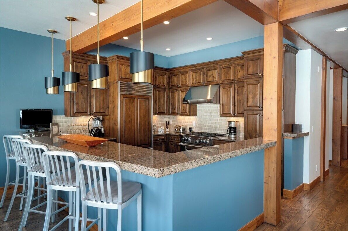 A modern kitchen with wooden cabinets, a granite countertop, and a central island with bar stools.