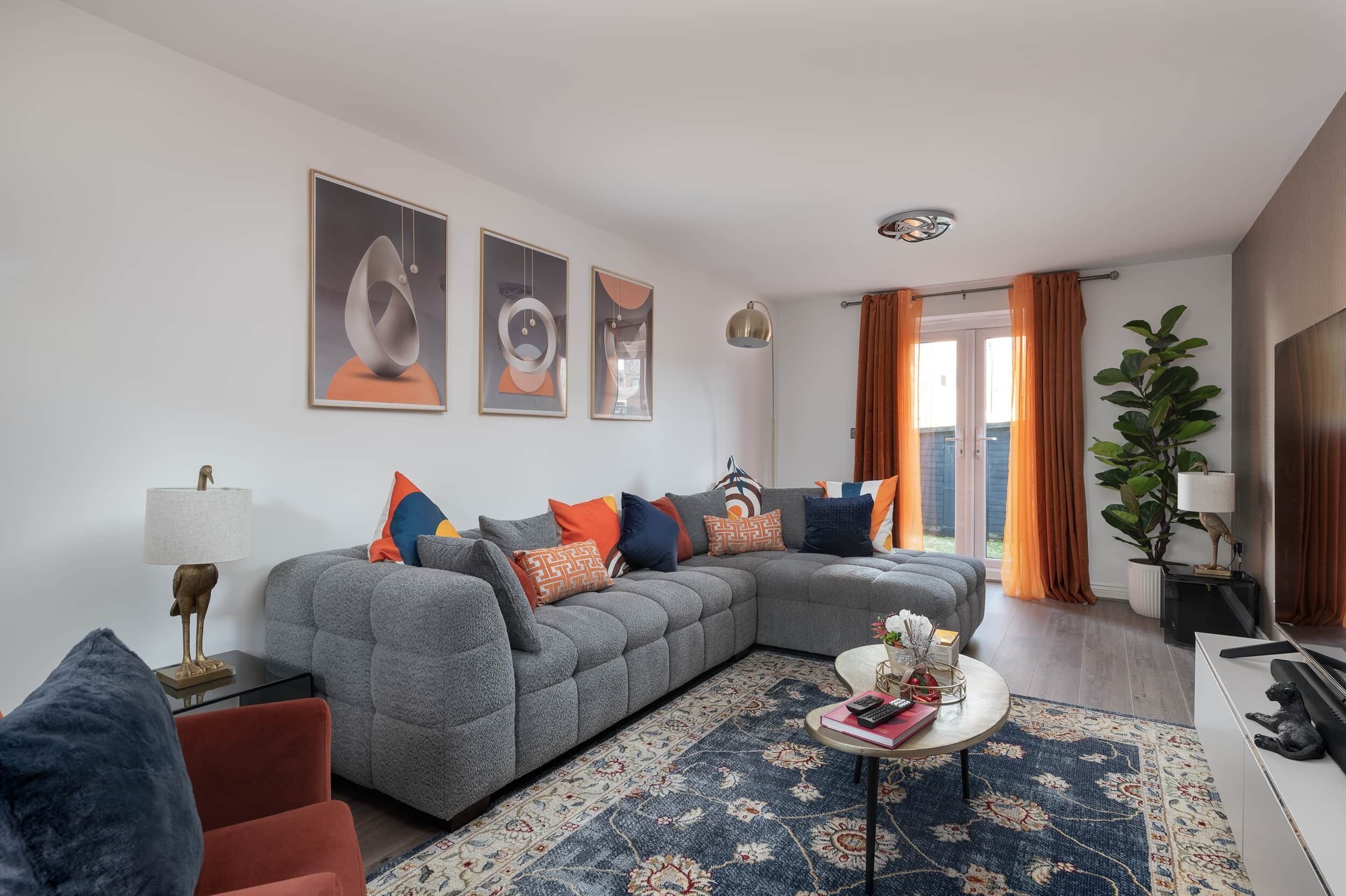 A modern living room with a grey sectional sofa, a patterned rug, and a large window with curtains.