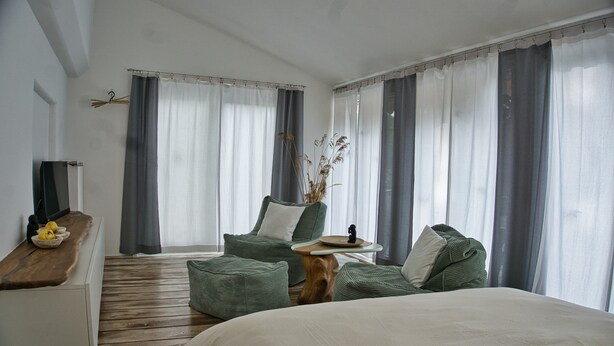 A modern hotel room with a large bed, a wooden desk, a green sofa, and a small table with a vase of dried plants. - Vacation apartment in the Allgäu (Aichstetten)