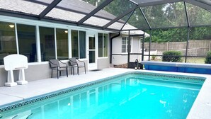 Ein Swimmingpool mit überdachter Terrasse, einer kleinen Sitzecke und Blick auf den Garten.