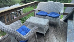 A wicker deck with two chairs and a table, surrounded by a wooden railing and a view of dense greenery. - Berkshires Barn Stay on Working Homestead  (West Stockbridge)