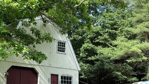 A white wooden barn with a red door and windows, surrounded by lush greenery and trees. - Berkshires Barn Stay on Working Homestead  (West Stockbridge)