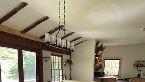 A dining area with a wooden table and black chairs, a kitchen area with a window, and a hanging light fixture. - Berkshires Barn Stay on Working Homestead  (West Stockbridge)