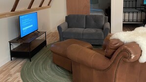 A living room with a brown leather sofa, a grey couch, and a television on a stand. - Berkshires Barn Stay on Working Homestead  (West Stockbridge)