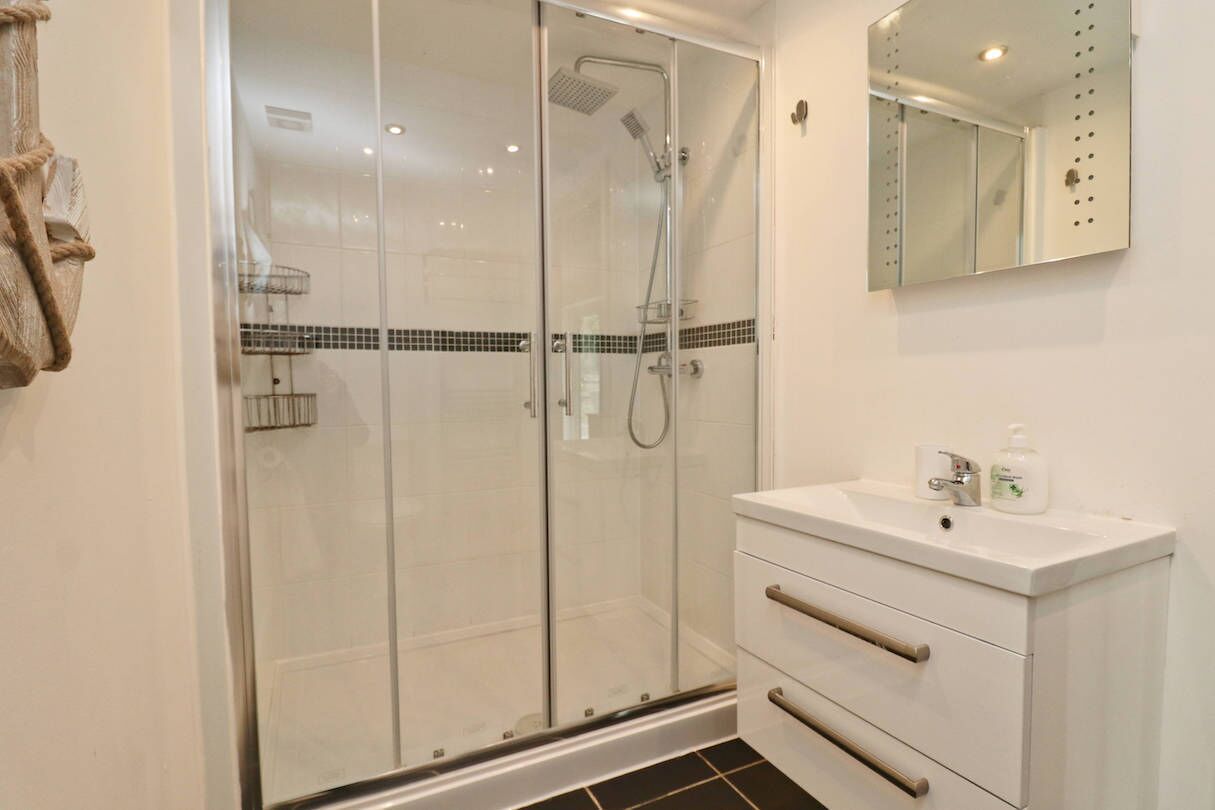 Une salle de bain moderne avec une douche à parois de verre, un meuble-lavabo blanc doté d’un miroir et un sol carrelé.