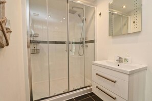 A modern bathroom with a glass-enclosed shower, a white vanity with a mirror, and a tiled floor. - Peaceful bungalow near to Constantine Bay, dog friendly with enclosed garden (Saint Merryn)