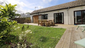 A house with a patio, wooden furniture, and a grassy garden. - Peaceful bungalow near to Constantine Bay, dog friendly with enclosed garden (Saint Merryn)