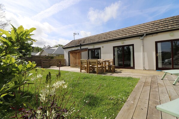 A house with a patio, wooden furniture, and a grassy garden. - Peaceful bungalow near to Constantine Bay, dog friendly with enclosed garden (Saint Merryn)