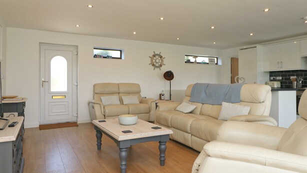 A spacious living room with a beige sofa set, a wooden coffee table, and a kitchen area in the background. - Peaceful bungalow near to Constantine Bay, dog friendly with enclosed garden (Saint Merryn)