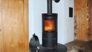 Un poêle à bois dont on peut voir les flammes à l’intérieur, installé dans une pièce aux murs en bois et au sol en pierre.