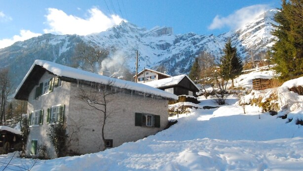 Un village de montagne enneigé, avec des maisons traditionnelles, un ciel dégagé et un sommet montagneux imposant en arrière-plan.