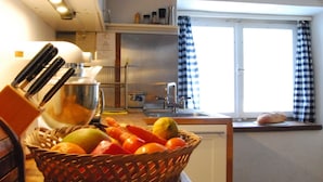 Une cuisine avec un panier de fruits, un évier et une fenêtre ornée de rideaux à carreaux.