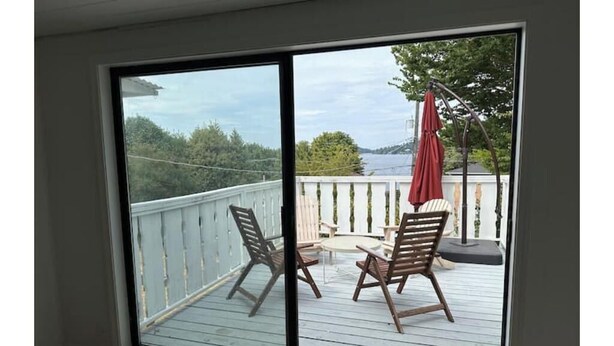A room with a sliding glass door leading to an outdoor deck with a view of a body of water and trees.
