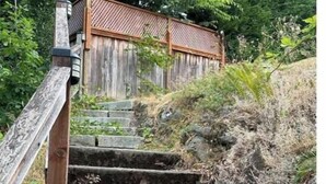 A set of stone steps leading up to a wooden structure with a lattice design, surrounded by greenery.