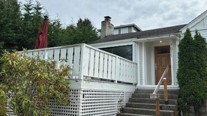 A house with a white exterior, a wooden deck, and a staircase leading to the front door.