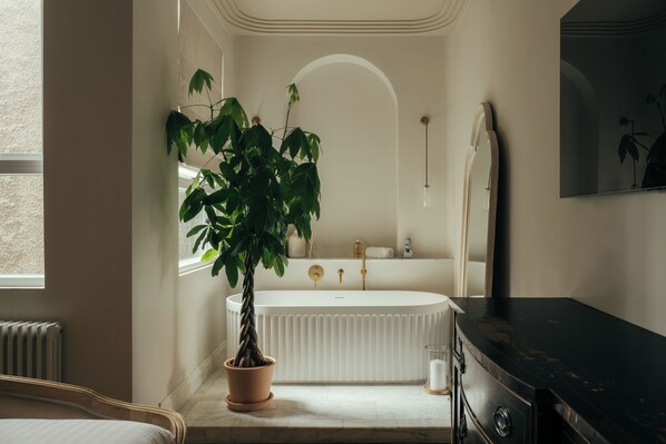 Ein Badezimmer mit freistehender Badewanne, einer Topfpflanze, einem Spiegel und einem Heizkörper.