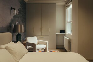 Ein Schlafzimmer mit Bett, Stuhl, Kleiderschrank, Lampe und Heizkörper.