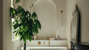 A bathroom with a white bathtub, a potted plant, a dresser, and a mirror.