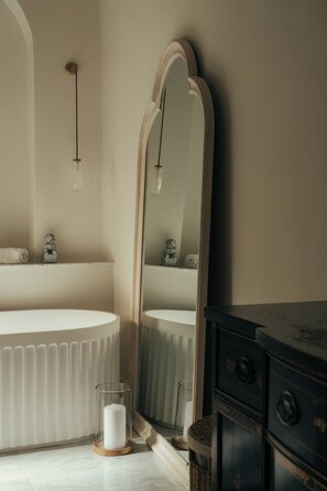 Ein Badezimmer mit einem großen Spiegel, einer runden Badewanne, einem Holzkabinent und einem Glas-Kerzenhalter.