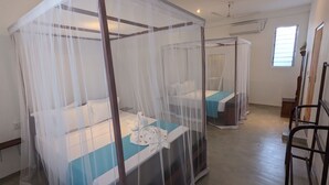 A hotel room with two beds, each covered with a mosquito net. There is a wooden chair and a small table in the room. - Hiriketiya Hideway  (Hiriketiya)