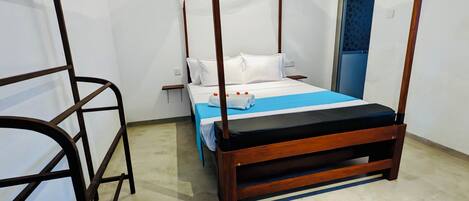 Una cama con dosel, con una colcha azul y almohadas blancas, una mesita de noche pequeña y un enchufe en la pared.