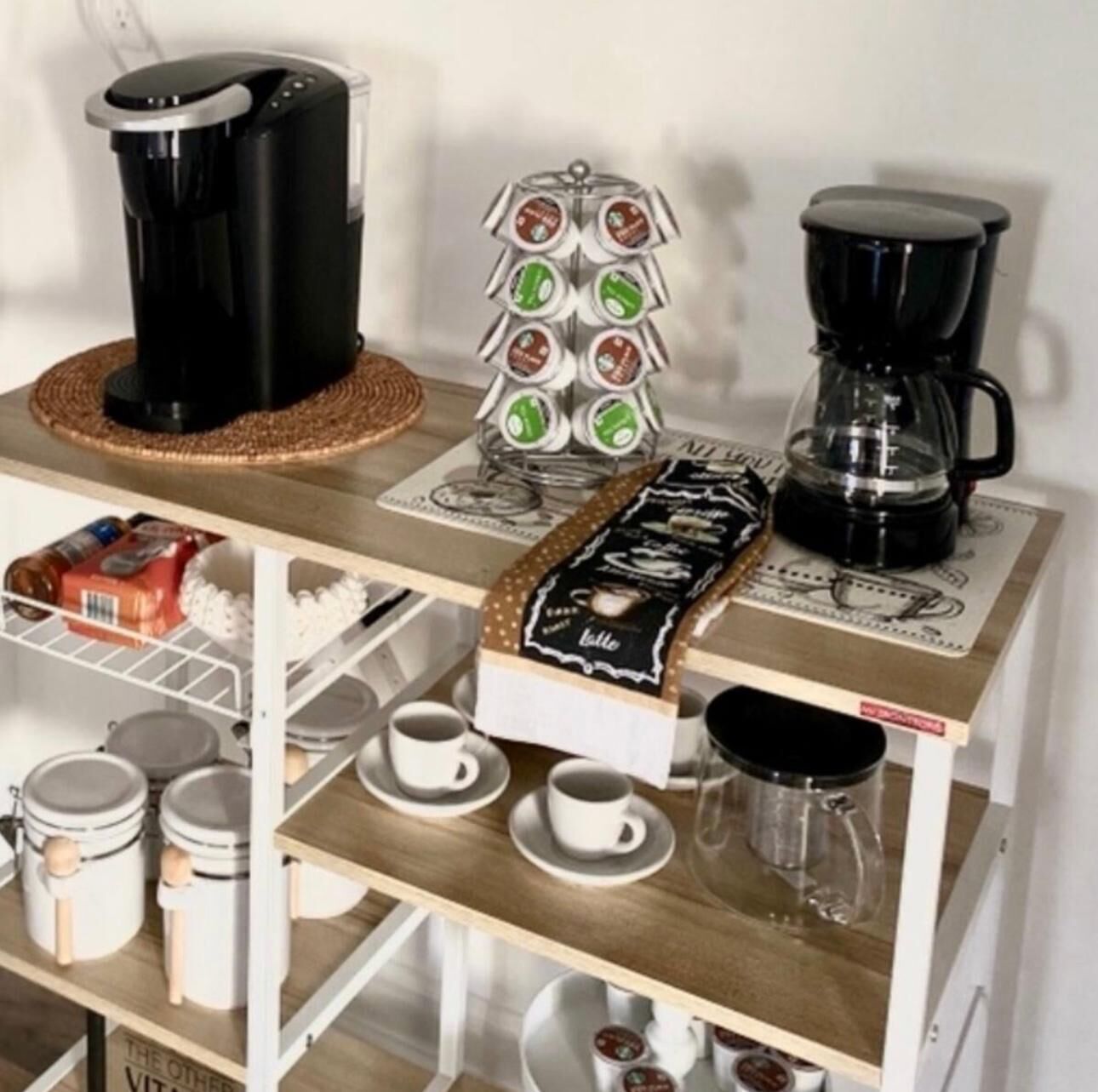 A coffee station with a coffee maker, a coffee pod dispenser, and a coffee pot on a wooden table.