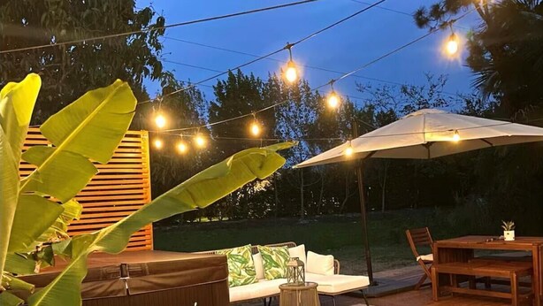 A wooden deck with outdoor furniture, string lights, and a large umbrella. - Pet-Friendly Estero Spacious House • Near FGCU, Beaches, RSW Airport & Hertz (Fort Myers)