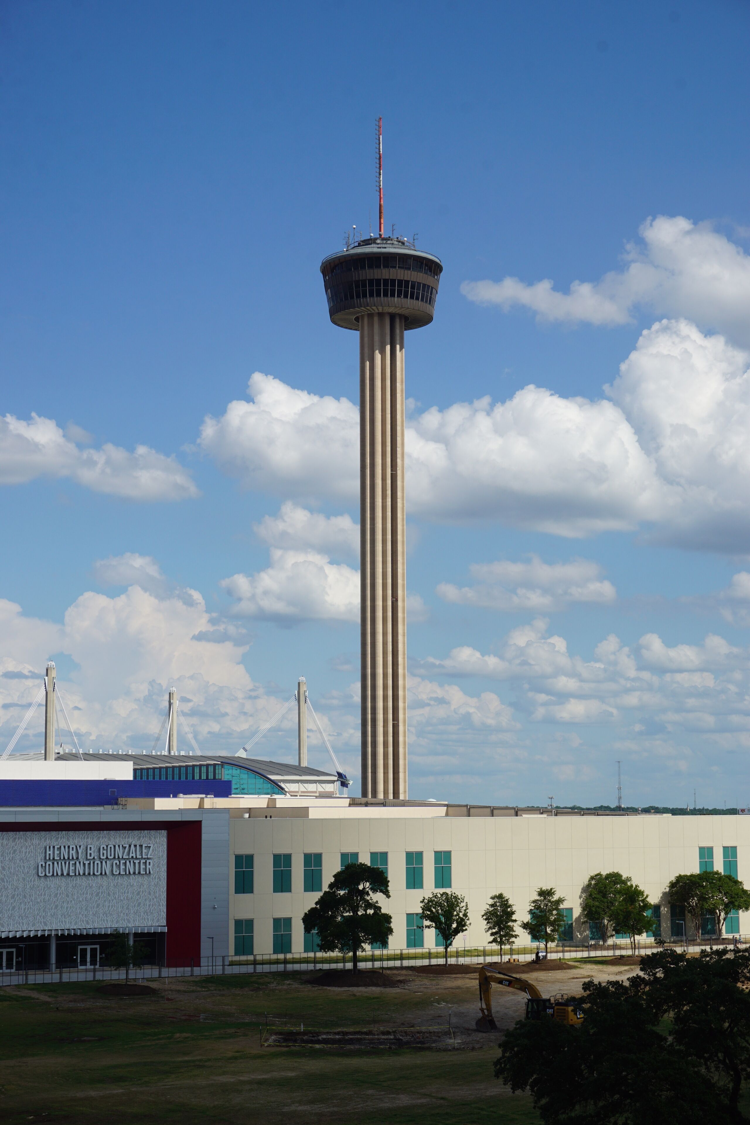 A tall tower with a control room at the top, a convention center building with a sign, and a clear blue sky with clouds.