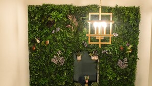 Una escalera con un muro verde cubierto de plantas, un farol colgante y una pequeña planta en maceta en el rellano.
