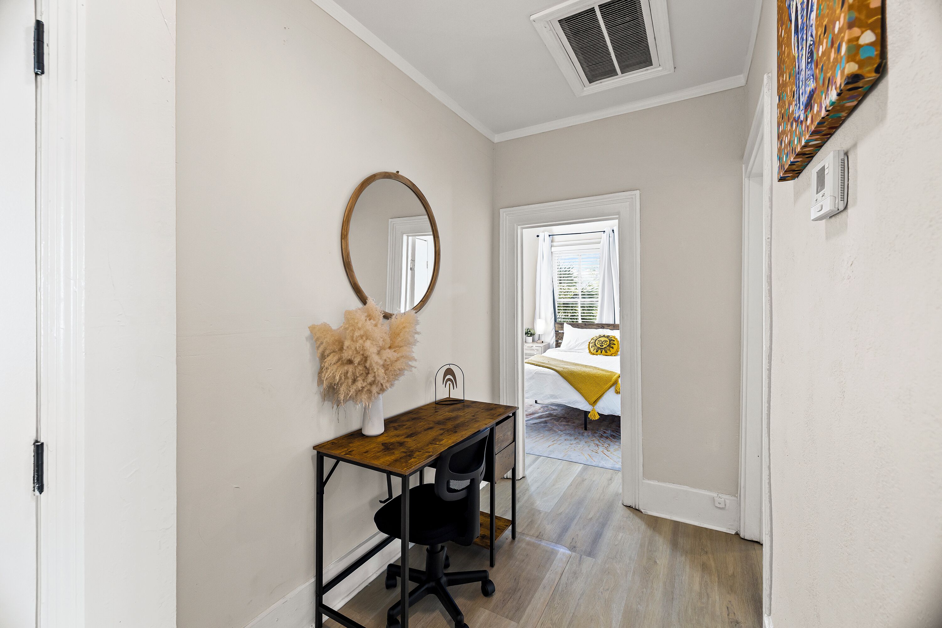A hallway with a desk, a mirror, and a door leading to a bedroom.