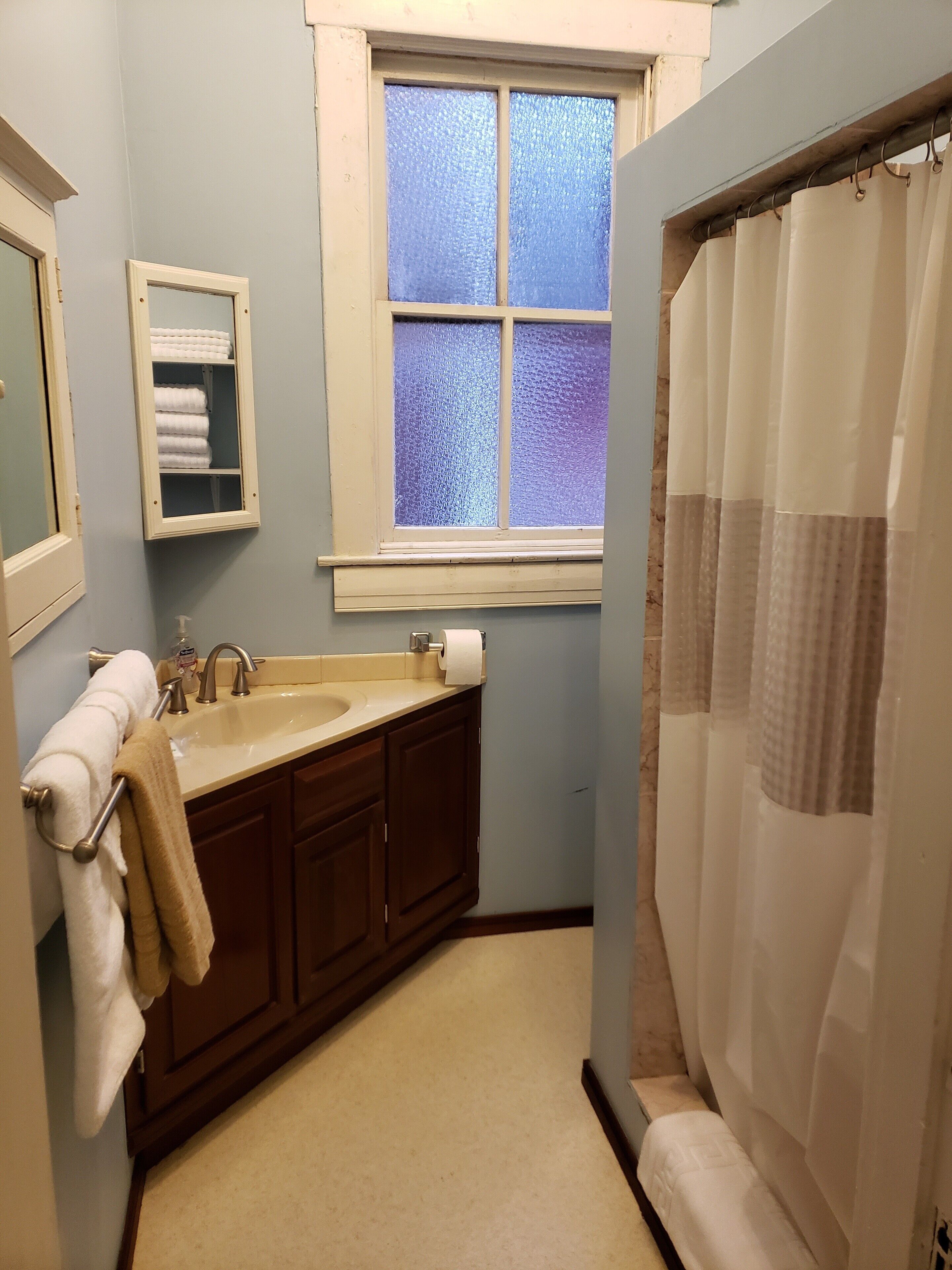 A bathroom with a sink, mirror, towel rack, and a window with frosted glass.