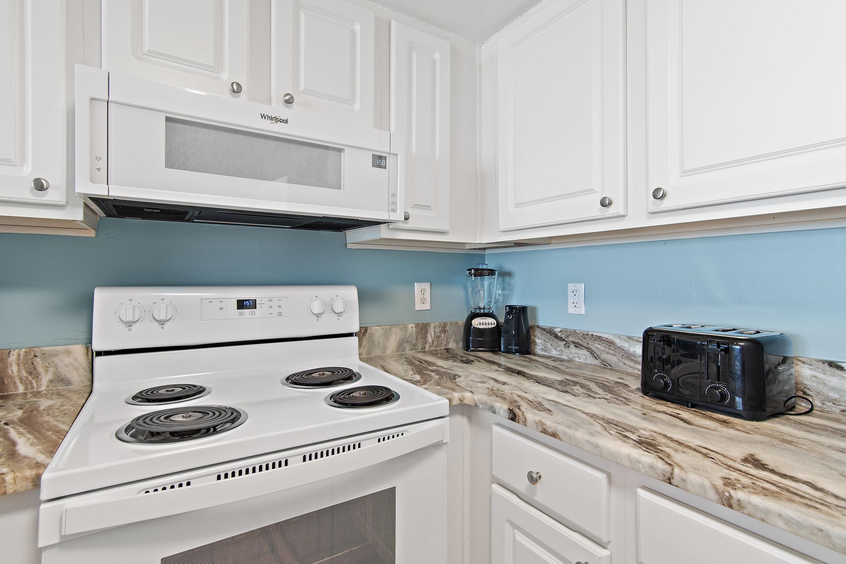 A kitchen with white cabinets, a white stove, a black toaster, and a blender on a marble countertop.