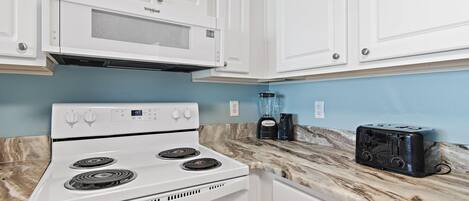 A kitchen with white cabinets, a white stove, a black toaster, and a blender on a marble countertop.