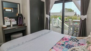 A bedroom with a bed, a dresser, a mirror, and a view of a balcony with outdoor furniture. - Coogee View (New Quay)