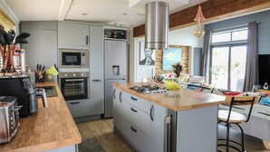 A modern kitchen with stainless steel appliances, a wooden island, and a large window providing natural light. - Coogee View (New Quay)