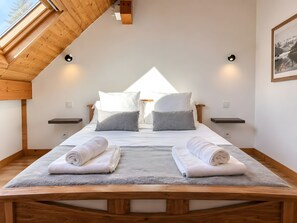 Une chambre avec un plafond en pente, un lit avec une literie blanche, deux tables de chevet et un tableau encadré au mur.