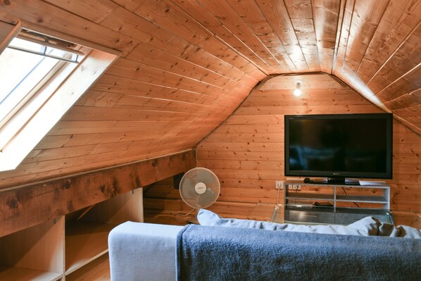 Une chambre mansardée chaleureuse avec des murs en bois, un téléviseur à écran plat, un ventilateur et un lit.