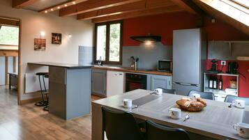 Une cuisine moderne avec des poutres en bois, un coin repas avec des chaises, un espace pour prendre le petit-déjeuner et un mur d’accent rouge.